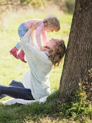 Mutter hebt Kind in die Luft unter Baum