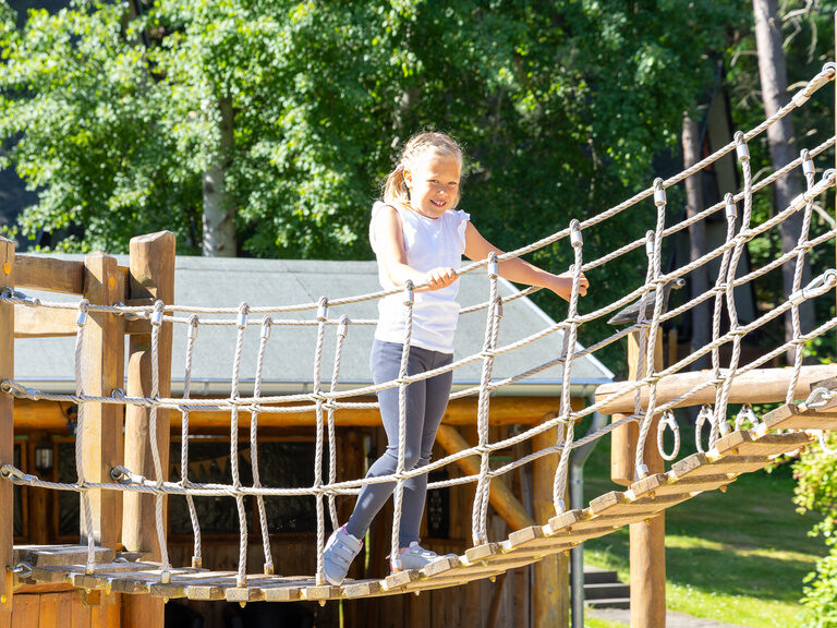 Kind überquert eine Hängebrücke auf dem Abenteuerspielplatz