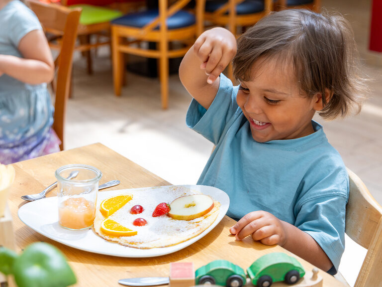 Kind genießt eine Mahlzeit mit Obst und Pfannkuchen - Kids All-Inclusive