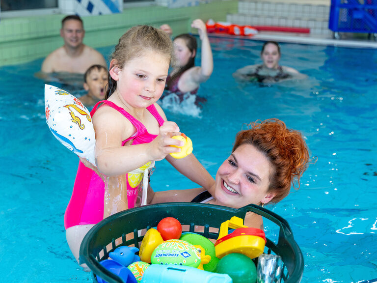 Kind mit Schwimmflügel und Spielzeug mit Frau im Schwimmbecken