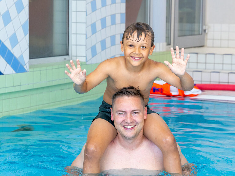 Kind sitzt auf Schultern des Vaters im Schwimmbecken