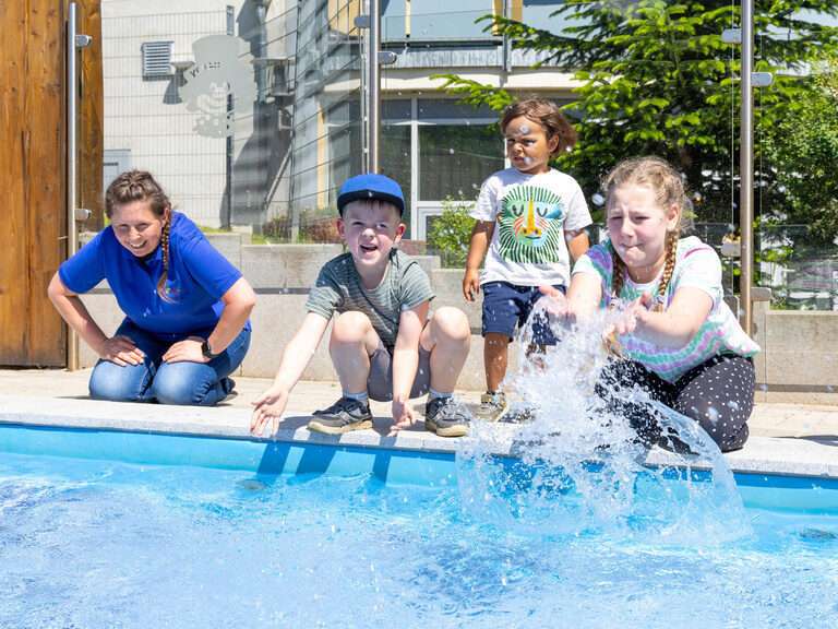 Kinder planschen mit einem Betreuer am Rand des Pools im Family Club Harz