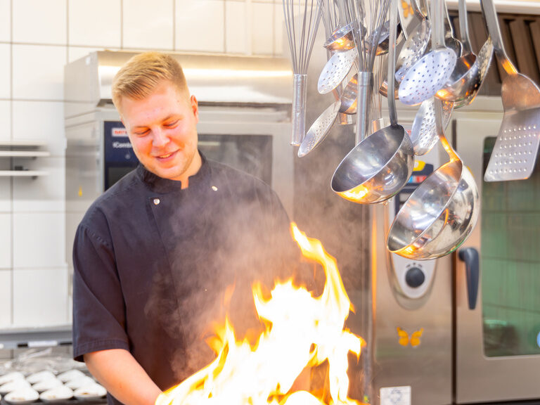 Koch bei der Zubereitung mit einer Pfanne, die in Flammen steht