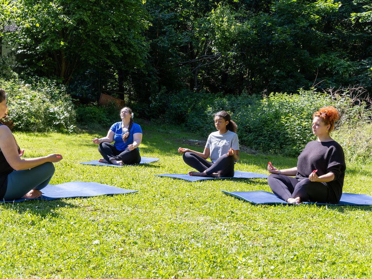 Yoga-Gruppe meditiert auf einer Wiese im Freien